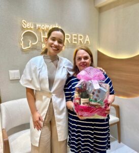 Dentista e paciente sorriem com cesta de presentes após tratamento de implante dentário na clínica Herrera Prime em São José dos Campos.