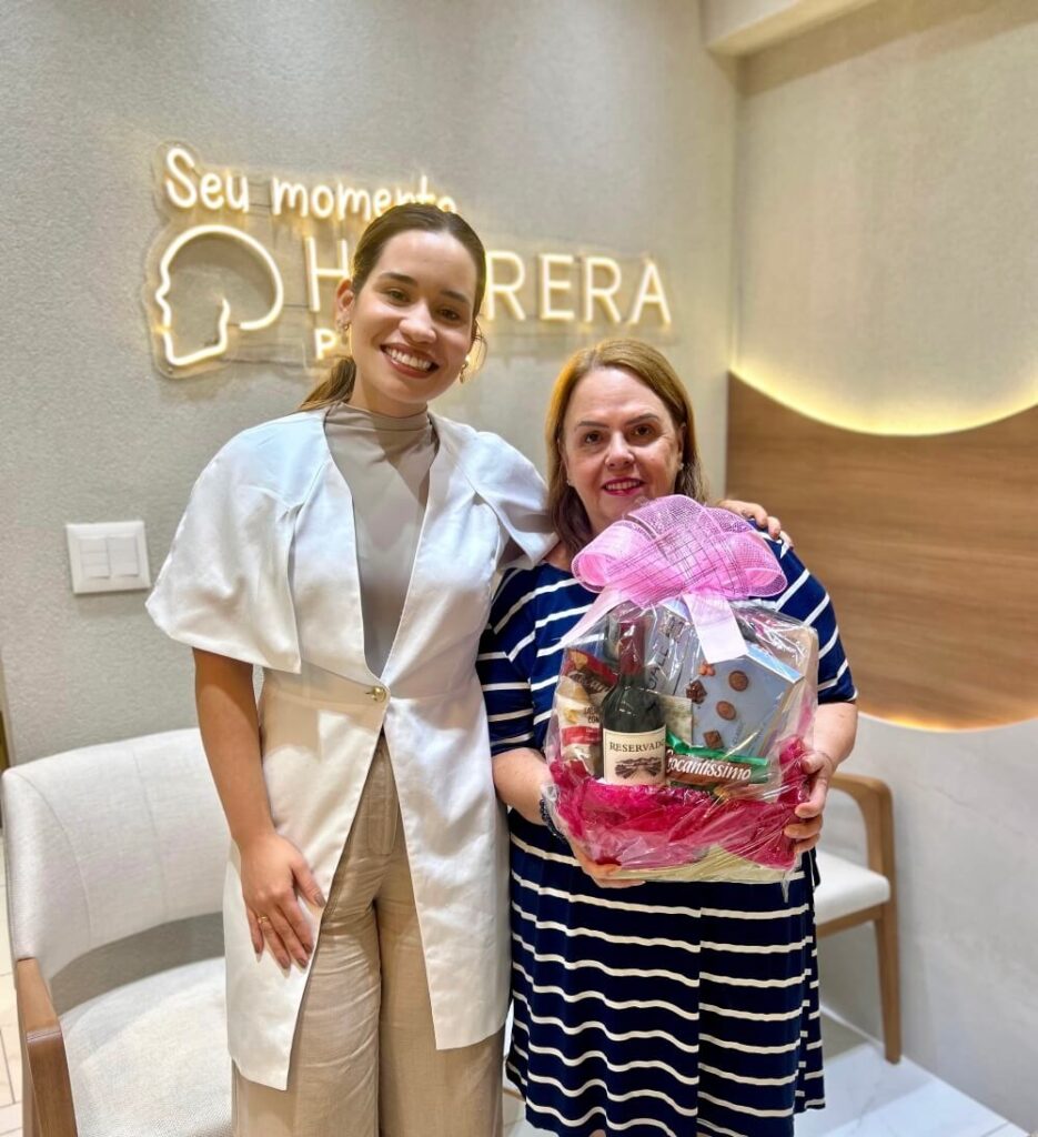 Dentista e paciente sorriem com cesta de presentes após tratamento de implante dentário na clínica Herrera Prime em São José dos Campos.