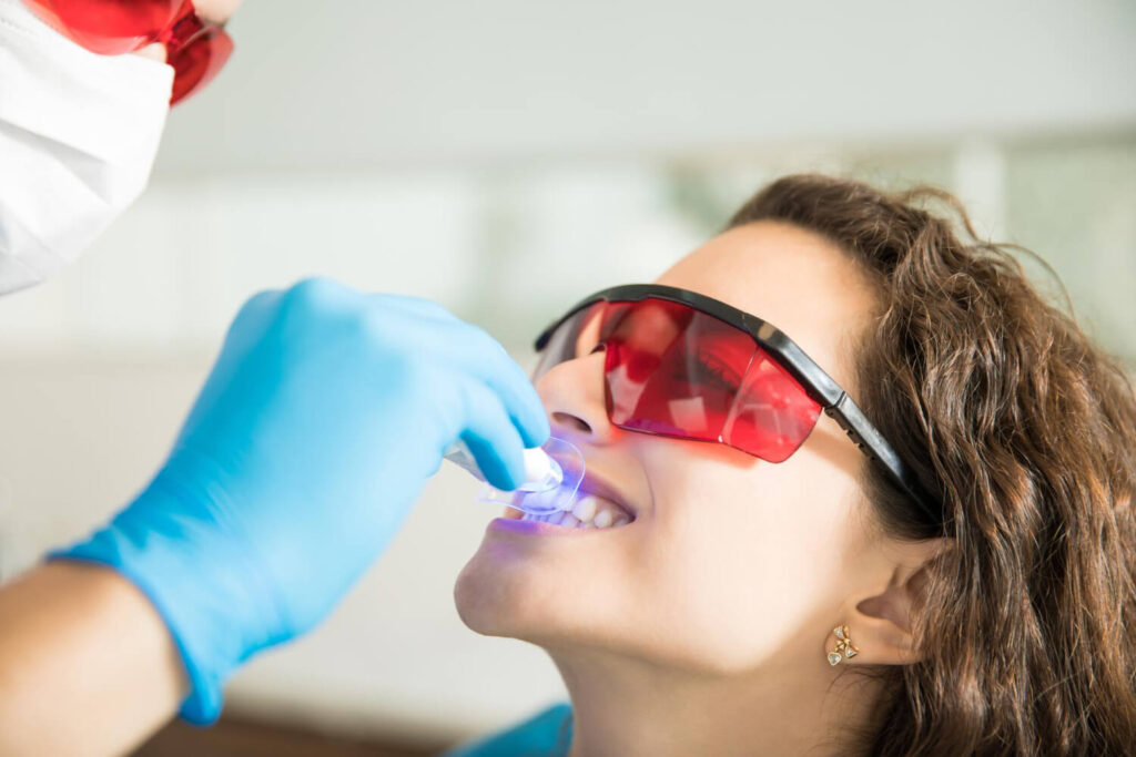 Paciente com óculos vermelhos protetores passa por clareamento dental a laser na Clínica Herrera Prime em São José dos Campos.
