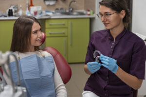 Dentista de óculos e jaleco roxo mostra alinhadores invisíveis para paciente na Clínica Herrera Prime em São José dos Campos.