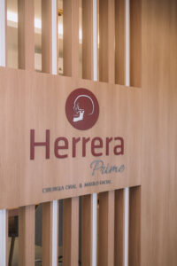 Logotipo da Herrera Prime em painel de madeira elegante na clínica odontológica em São José dos Campos com foco em cirurgia bucomaxilofacial.